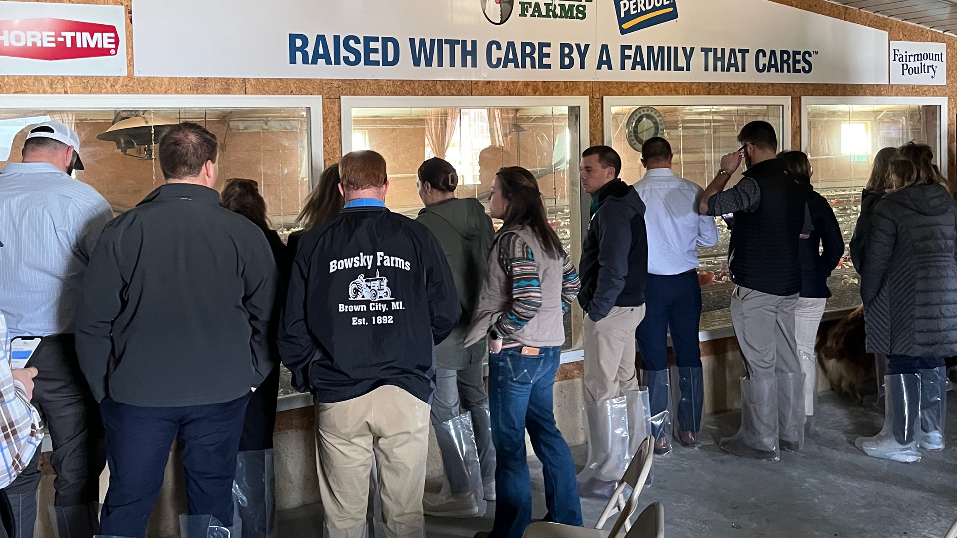 A group of young farmers looking through the observation window of Cooley Farms under a sign that reads "RAISED WITH CARE BY A FAMILY THAT CARES."