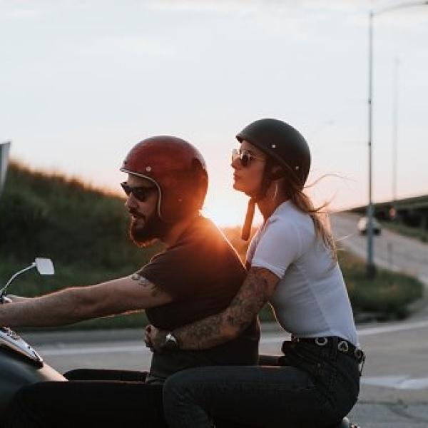 couple ride a motorcycle with the sunset behind them