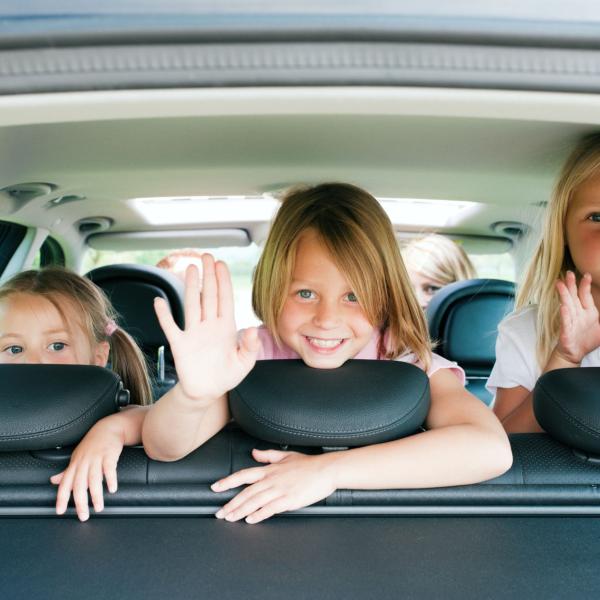 3 little girls wave from backseat of car