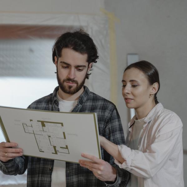A husband in wife look at blueprints in a room under repairs