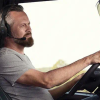 Profile view of a man at the wheel of a semi truck while wearing a BlueParrott headset and keeping his eyes on the road.